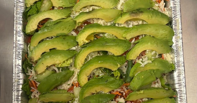 Dish served in a foil pan and topped with avocado slices