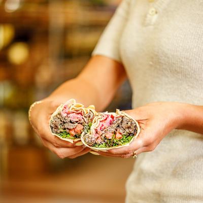 A person holding a beef shawarma wrap cut in half.