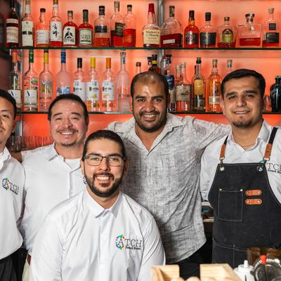 Staff posing behind a bar filled with various spirit bottles.