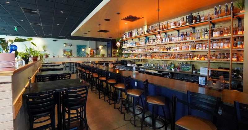 Interior, a long wooden bar top, black bar stools, shelves filled with liquor bottles,