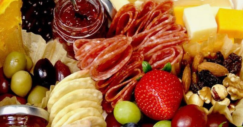 Close up of a platter with charcuterie, cheese, fruits, olives, jam, and nuts