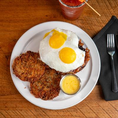 Breakfast sandwich topped with sunny side up eggs, served with hash browns.