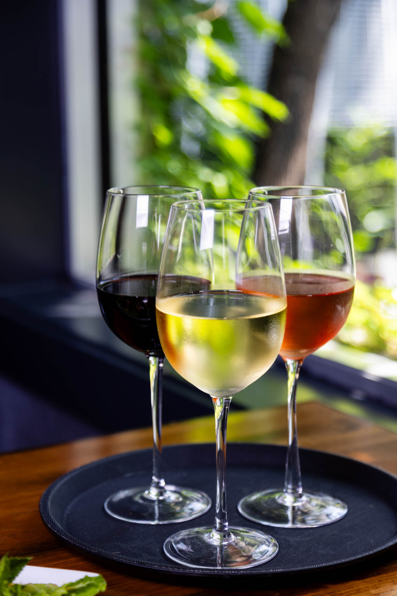 Three wine glasses filled with red, white, and rosé wine sit on a dark tray