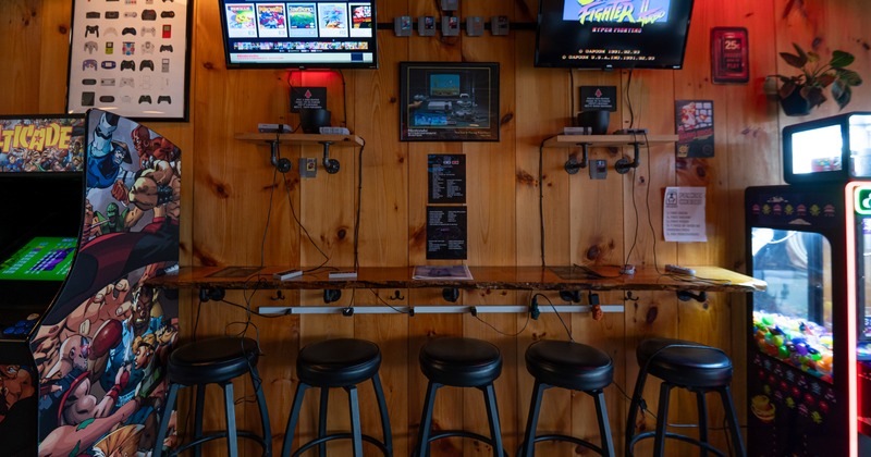 Bar table, bar stools, tv screens on the wall above