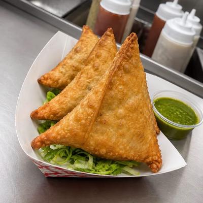 Samosas served on a bed of shredded lettuce with a small container of green chutney.