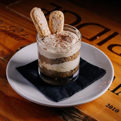 A serving of tiramisu presented in a glass on a wooden table.