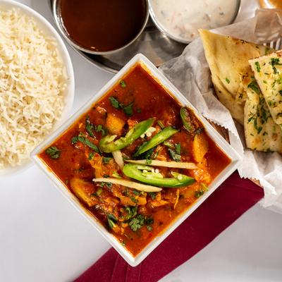 Chicken Vindaloo on a table with steamed rice, garlic naan, and sauces.
