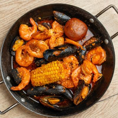 A pan with seafood boil includes corn on the cob, shrimp, mussels, and a boiled potato.