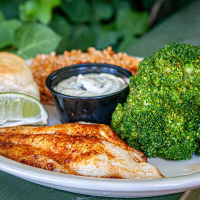 Grilled meat, green vegetables, white dip, lemon on the side.