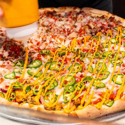 Large half-and-half pizza with jalapenos being drizzled with orange sauce.