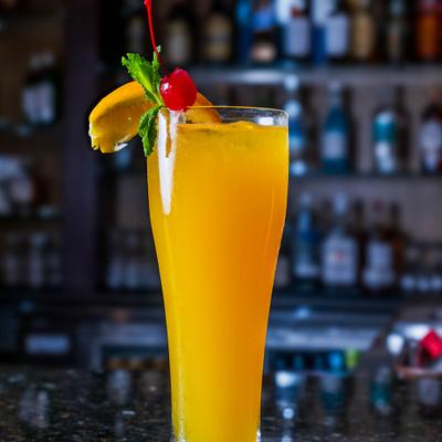Tall orange cocktail garnished with cherry, mint, and orange slice.