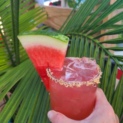 A refreshing red drink rimmed and garnished with a slice of watermelon.