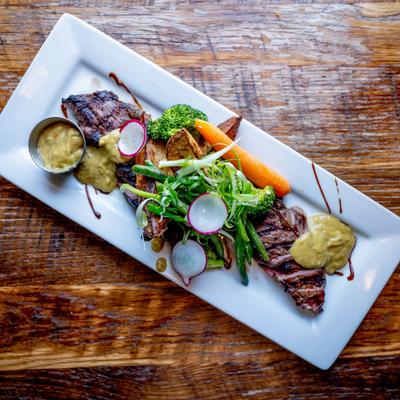A rectangular white plate holds carne asada steak, vegetables, and sauce.