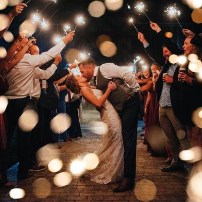 Newlywed couple kissing surrounded by guests holding sparklers at night.