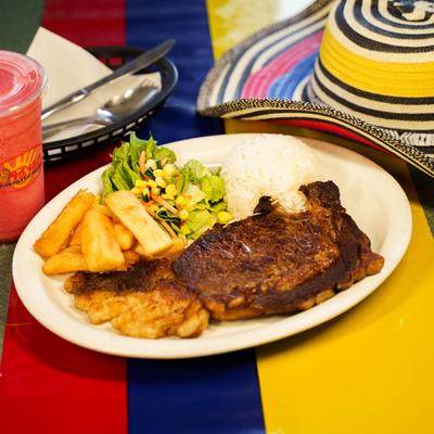 Grilled ribeye steak served with white rice, salad, and fried green plantains.