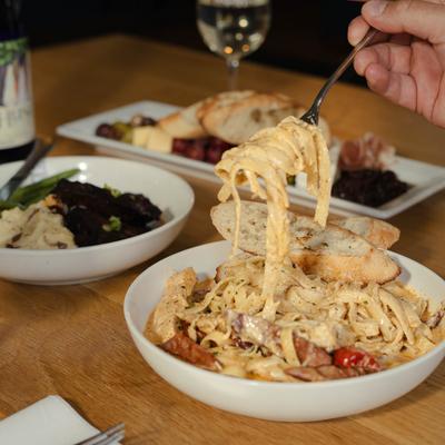 A hand is lifting a forkful of pasta above the bowl.