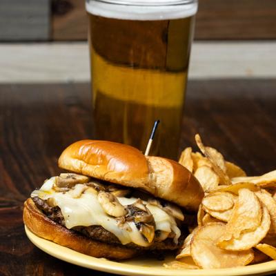 Mushroom Swiss Burger servd with chips and a glass of beer.