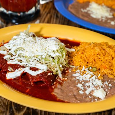 Enchiladas smothered in red sauce, with sour cream, cheese, lettuce, rice, and beans.