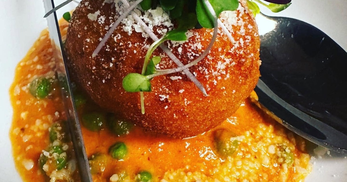 Arancini served on a bed of sauce, topped with grated cheese and micro greens