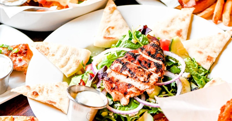 Mixed salad topped with grilled chicken and served with triangle pita bread and sauces