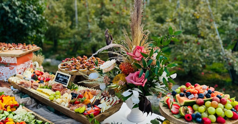 Outdoor wedding grazing table with fruits, meats, cheeses, and flowers