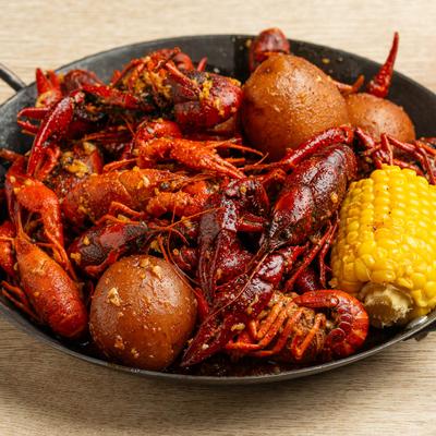 Black skillet filled with seasoned crawfish, corn on the cob, and potatoes on a wooden table.