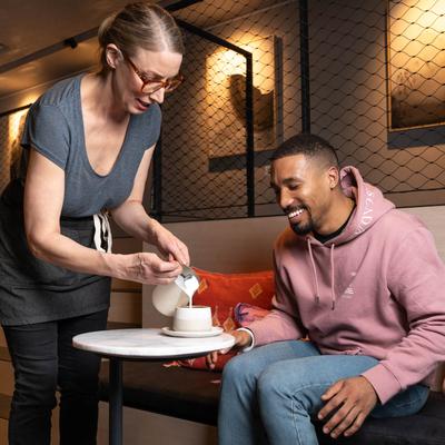 Lounge seating area, a waitperson serves coffee to a friendly guest.