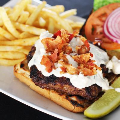 Blackened chicken sandwich with bacon and creamy sauce, served with fries.