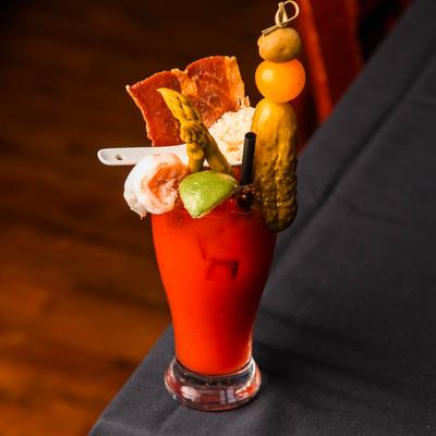 Amore Caesar cocktail garnished with shrimp, bacon, a lime wedge, and veggies on a dark tablecloth.