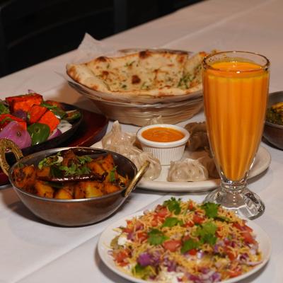 A variety of Indian dishes served on a white tablecloth with a glass of Mango Lassi.