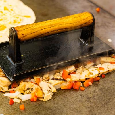 Chicken, onions, and peppers pressed on a hot griddle with a metal press.