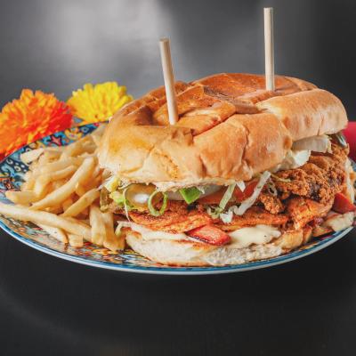 A large, loaded chicken sandwich served with french fries on a decorative plate.