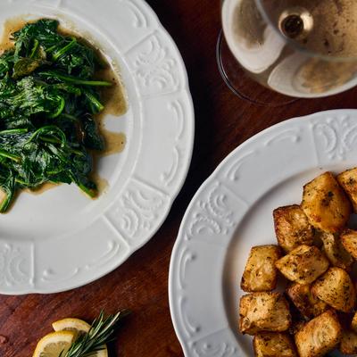 Sauteed greens alongside roasted potatoes on white plates.