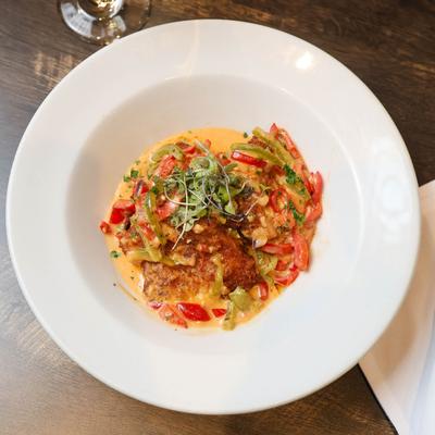 Lightly browned chicken topped with  microgreens, with  peppers on a creamy sauce.