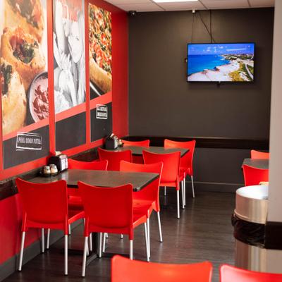 Casual restaurant dining area with red chairs, food posters, and a TV.