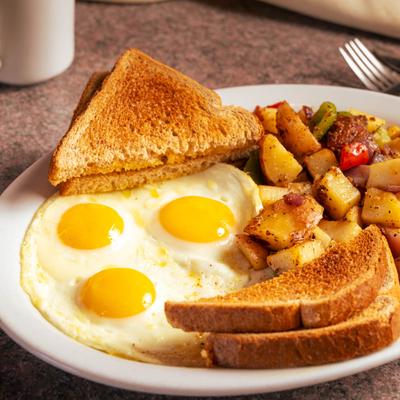 Three sunny-side-up eggs, crispy toast, and seasoned breakfast potatoes on a white plate.