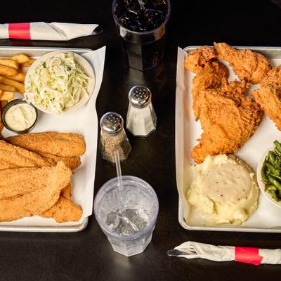 Catfish plate with sides served alongside fried chicken plate and two drinks.