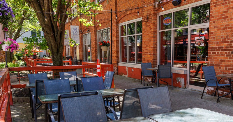 Outdoor dining area - tables, chairs, and a tree beside a red-brick building with large windows