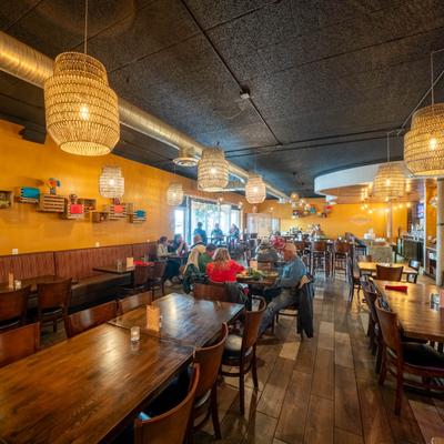 Dining area with wooden tables, woven pendant lights, and seated guests.