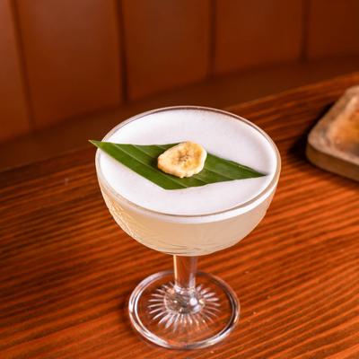 Frothy cocktail with a banana slice on a leaf garnish.