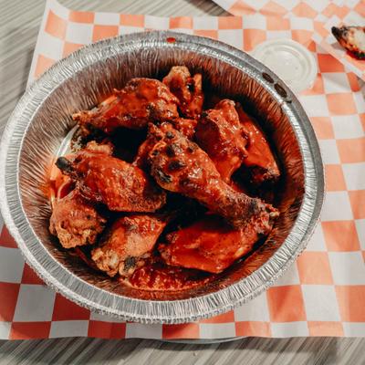 A round foil tray filled with spicy red buffalo chicken wings on a checkered paper.