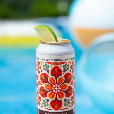 Floral design beer can with lime garnish with poolside water in the background.