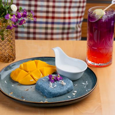 Mango sticky rice served with a sauce on the side and a cocktail.