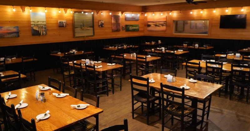 A warmly lit restaurant - wooden tables, black chairs, decorated with paintings and string lights
