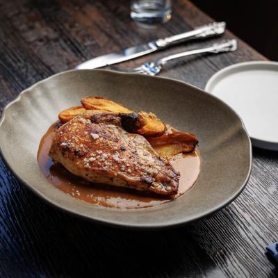 Seared poultry breast with fried potatoes in brown sauce on a gray plate..