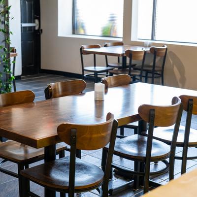 Dining area with wooden tables and chairs, natural light comes through large windows.