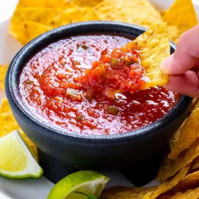Hand dipping tortilla chips into red salsa, close-up.