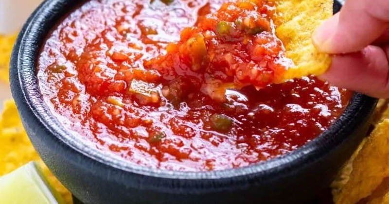 Tortilla chips being dipped into red salsa