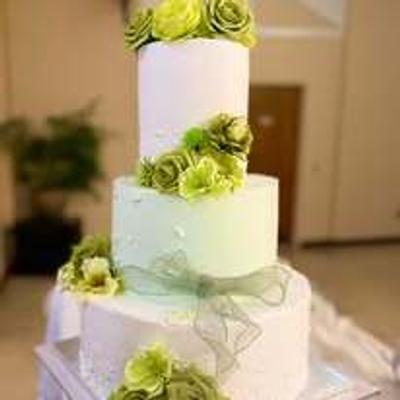 Three-tier white wedding cake decorated with sage green roses and ribbons.