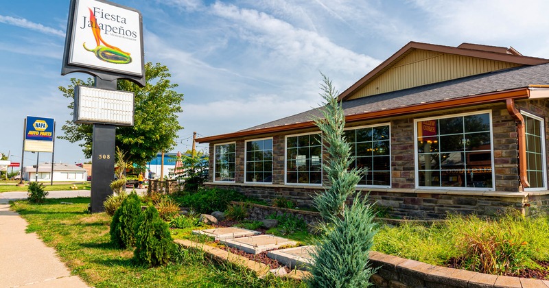 Restaurant building, greenery, "Fiesta Jalapenos" sign, windows, sidewalk